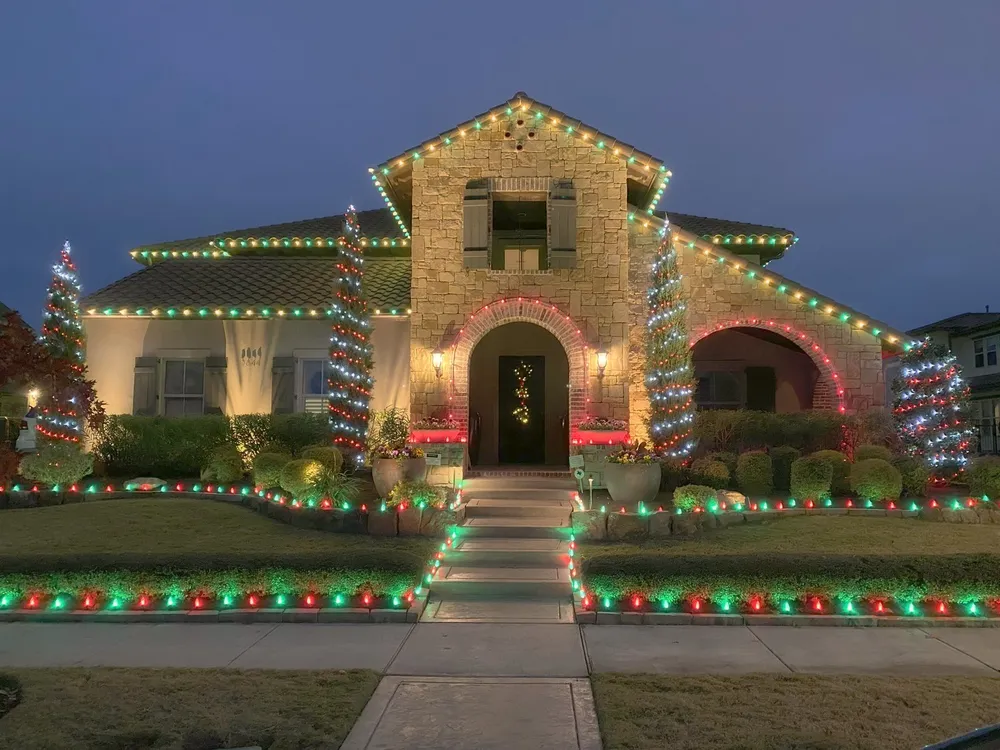 A North Texas home fully lit for Christmas across the roofline, trees, and walkway at blue hour