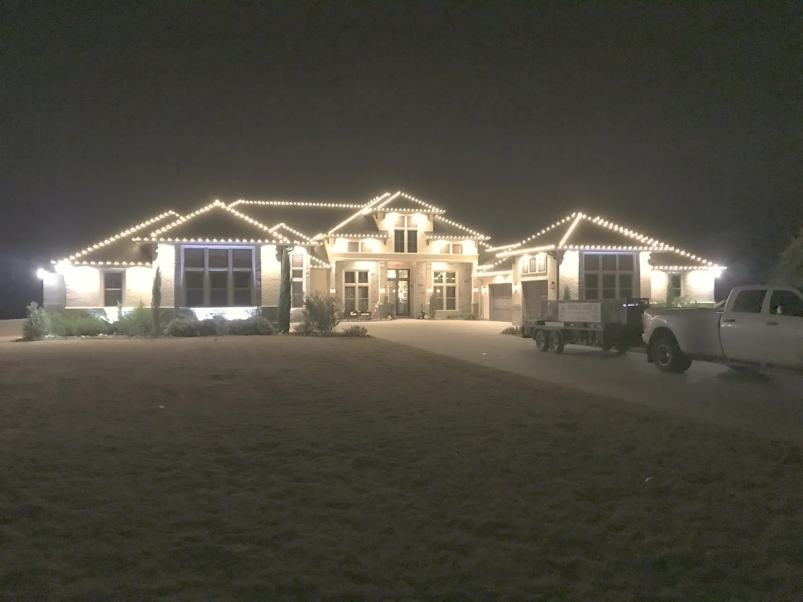 A long ranch roofline outlined in warm white Christmas lights across a North Texas property at night