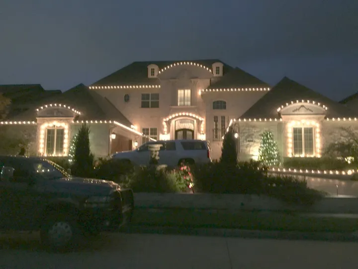 Warm white C9 Christmas lights along every roofline and peak of a North Texas stone home at night