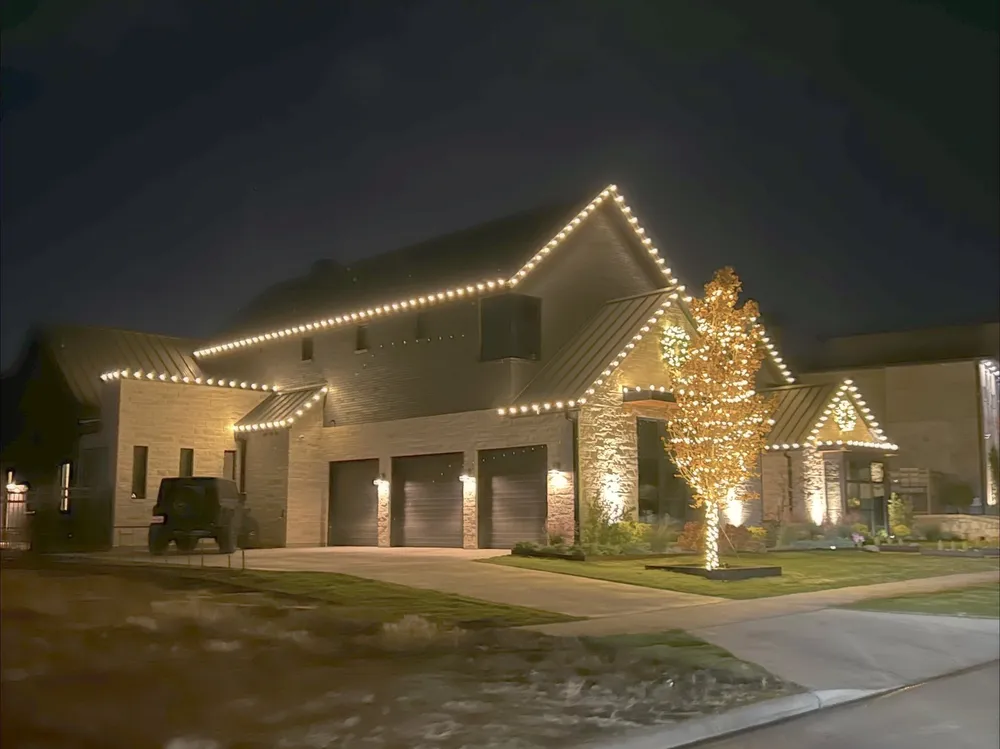 A two-story North Texas home lit at dusk with wrapped trees
