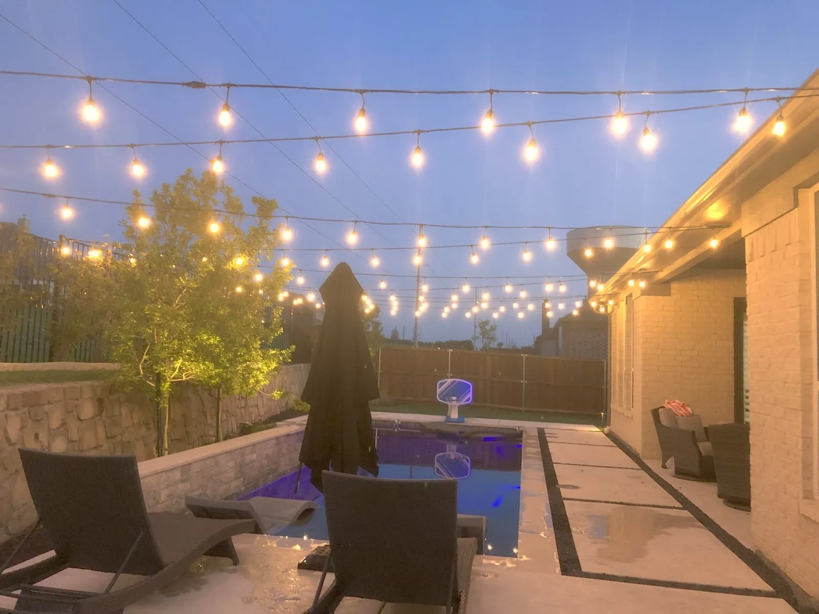 Bistro string lights strung over a patio and pool at dusk at a North Texas property